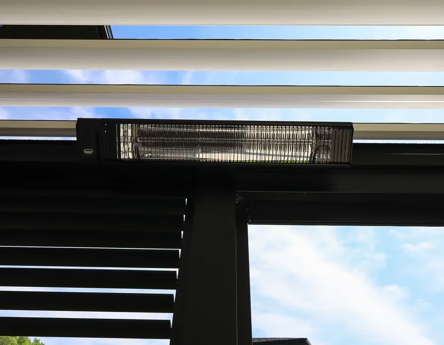 Gros plan d’un chauffe-terrasse électrique fixé sous une poutre : le tube à filament de carbone et son réflecteur dans le boîtier