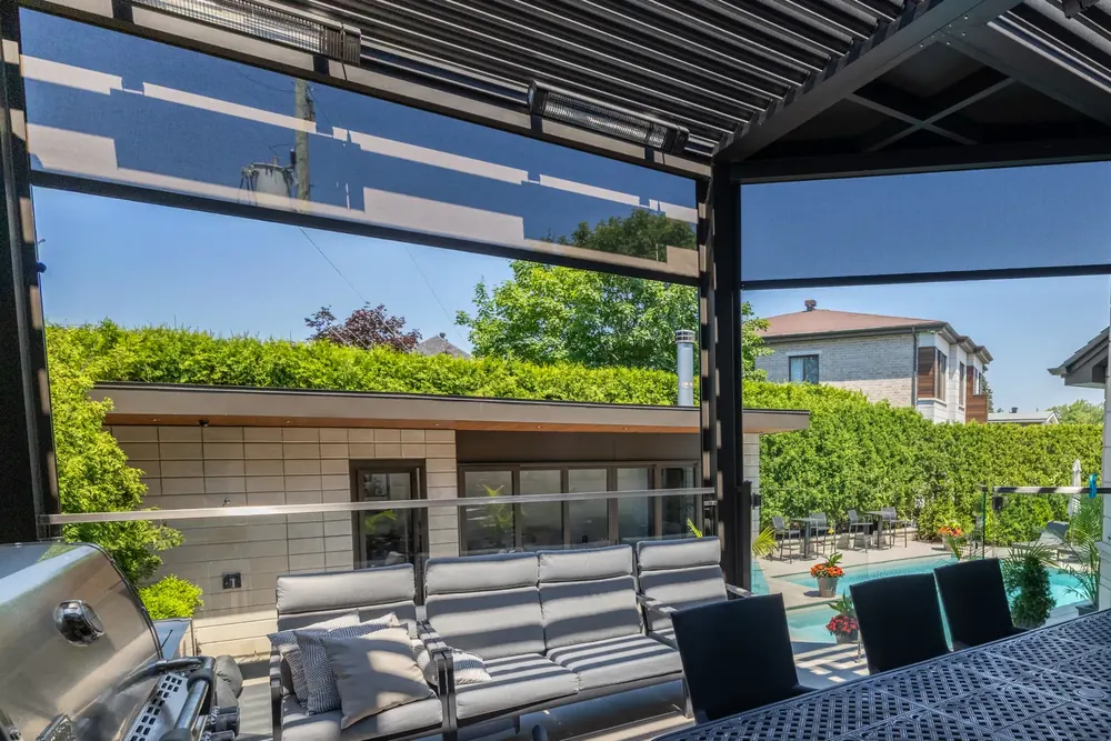 Deux chauffe-terrasse électriques fixés sous la poutre d’une pergola bioclimatique, toile solaire descendue derrière, piscine au fond