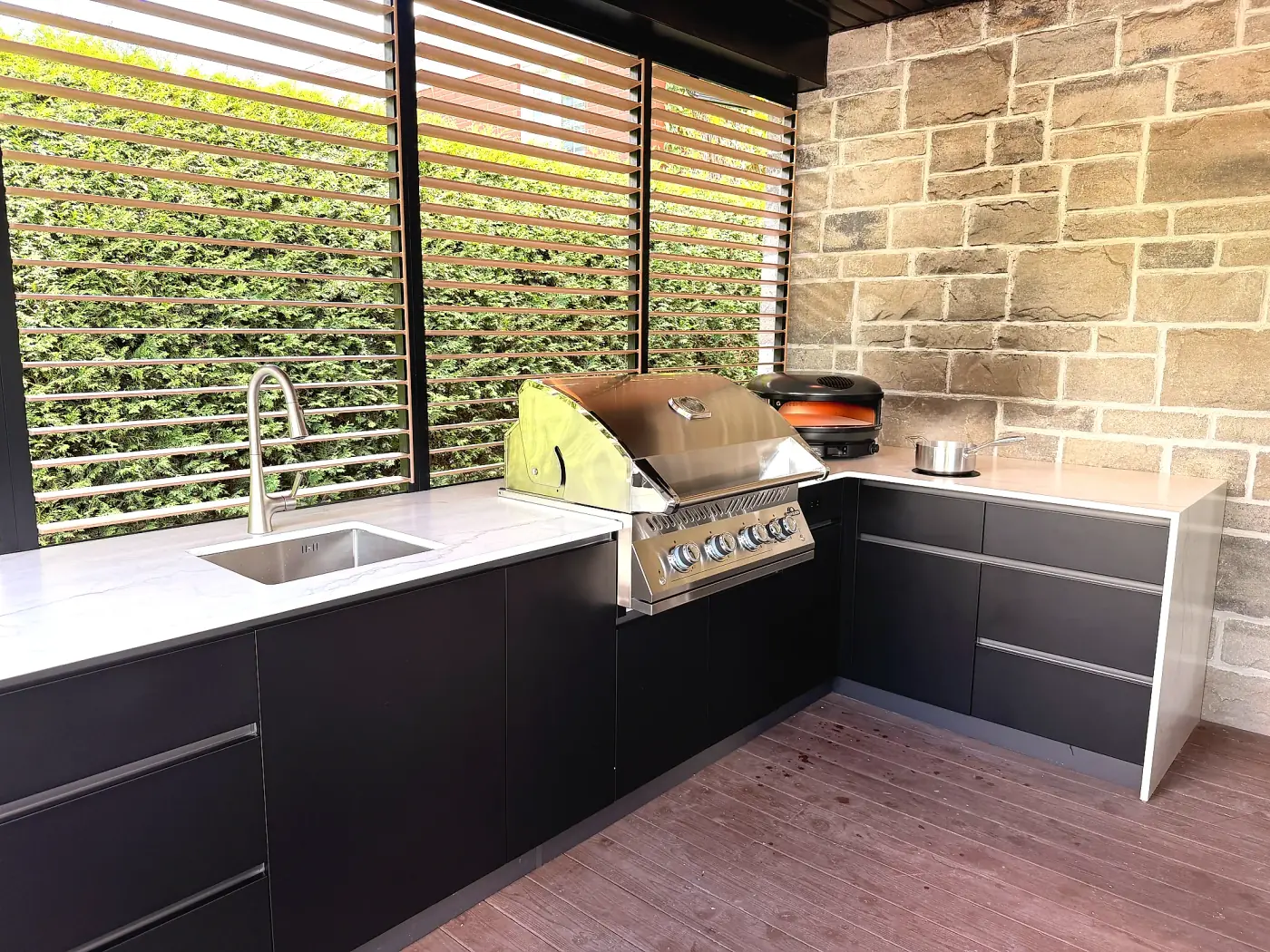 Custom outdoor kitchen: black stainless steel cabinets, sintered stone countertop, built-in barbecue and pizza oven under a covered terrace