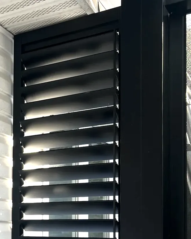 Détail d'un mur d'intimité : lames d'aluminium noir dans leur cadre, lumière rasante sur le profil des lames