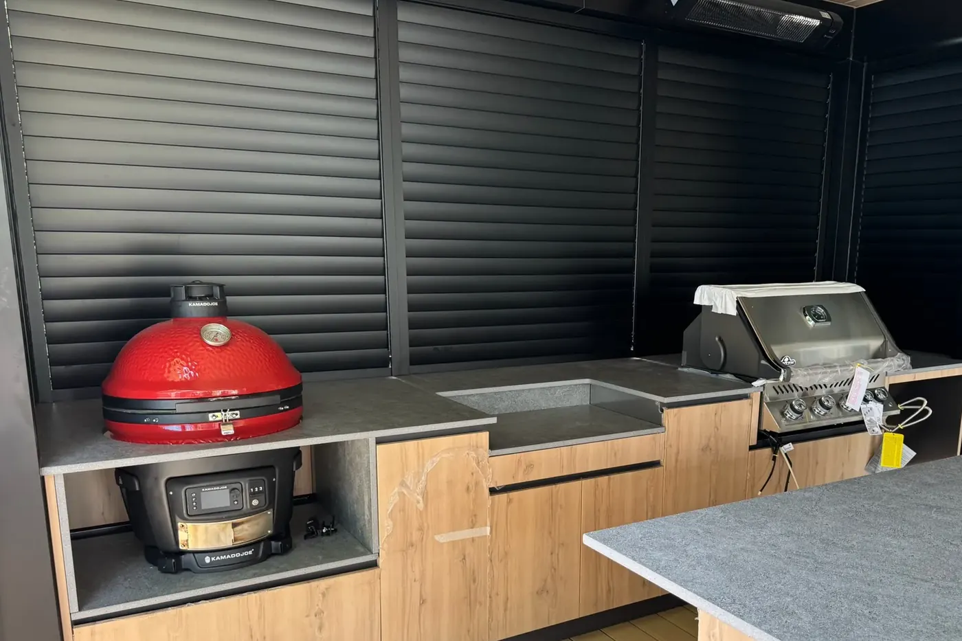 Cuisine extérieure abritée par un mur d'intimité en persiennes d'aluminium noir, lames fermées