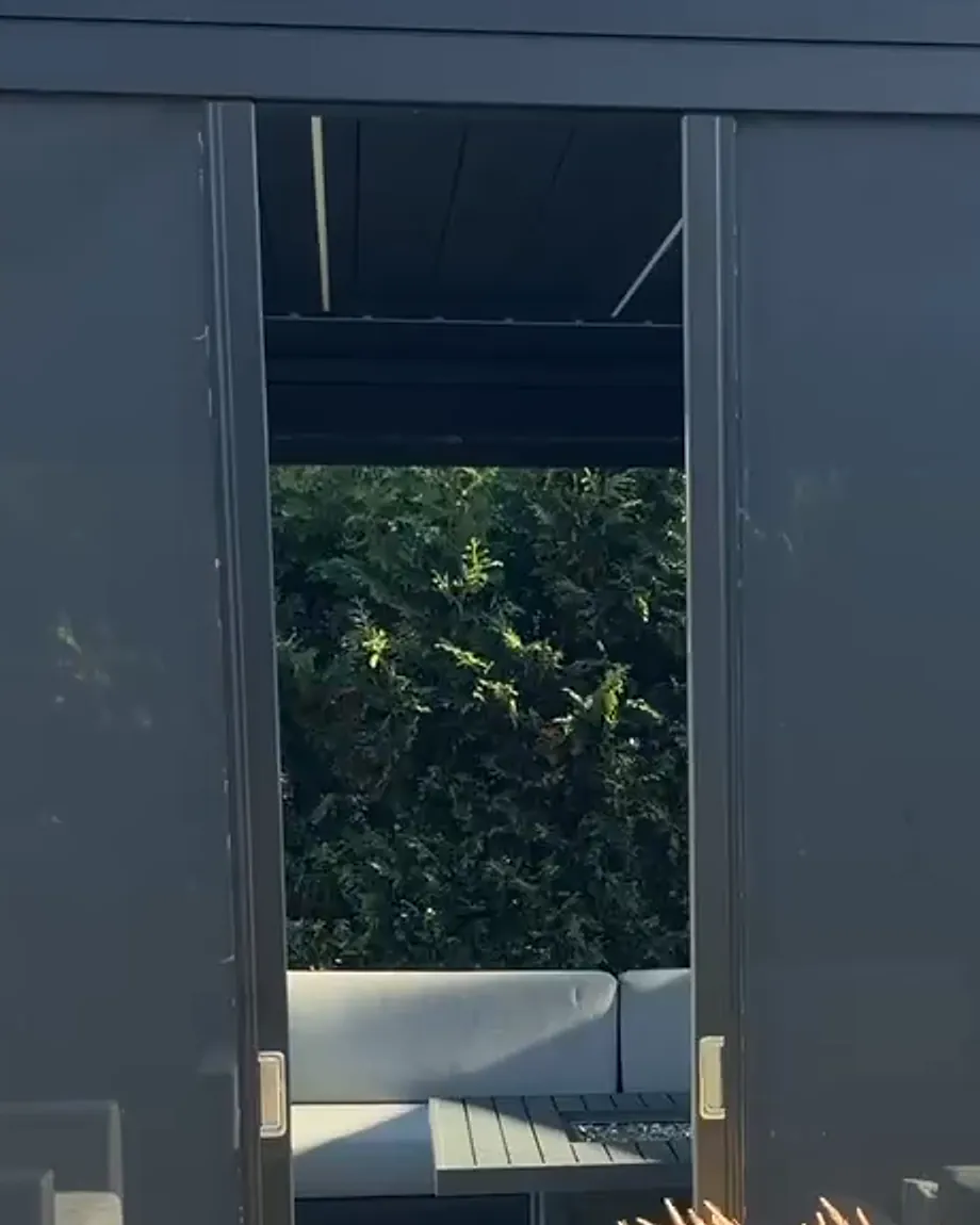 Horizontal solar shade seen full height: the top rail, the two operating bars parted at the centre and the bottom rail on the ground, with the outdoor lounge in the opening