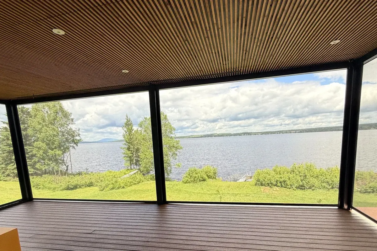 Vue panoramique sur le lac Saint-François à travers les toiles solaires, depuis l’espace de vie couvert au plafond de lattes de bois