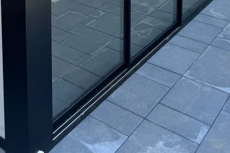Rail encastré à deux glissières au pied du verre coulissant, sur une terrasse en dalles de pierre