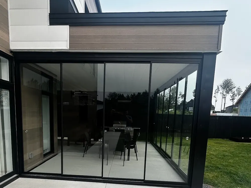Angle d'une enceinte vitrée vue de la dalle : les panneaux se referment sur la façade et sur le côté de la maison