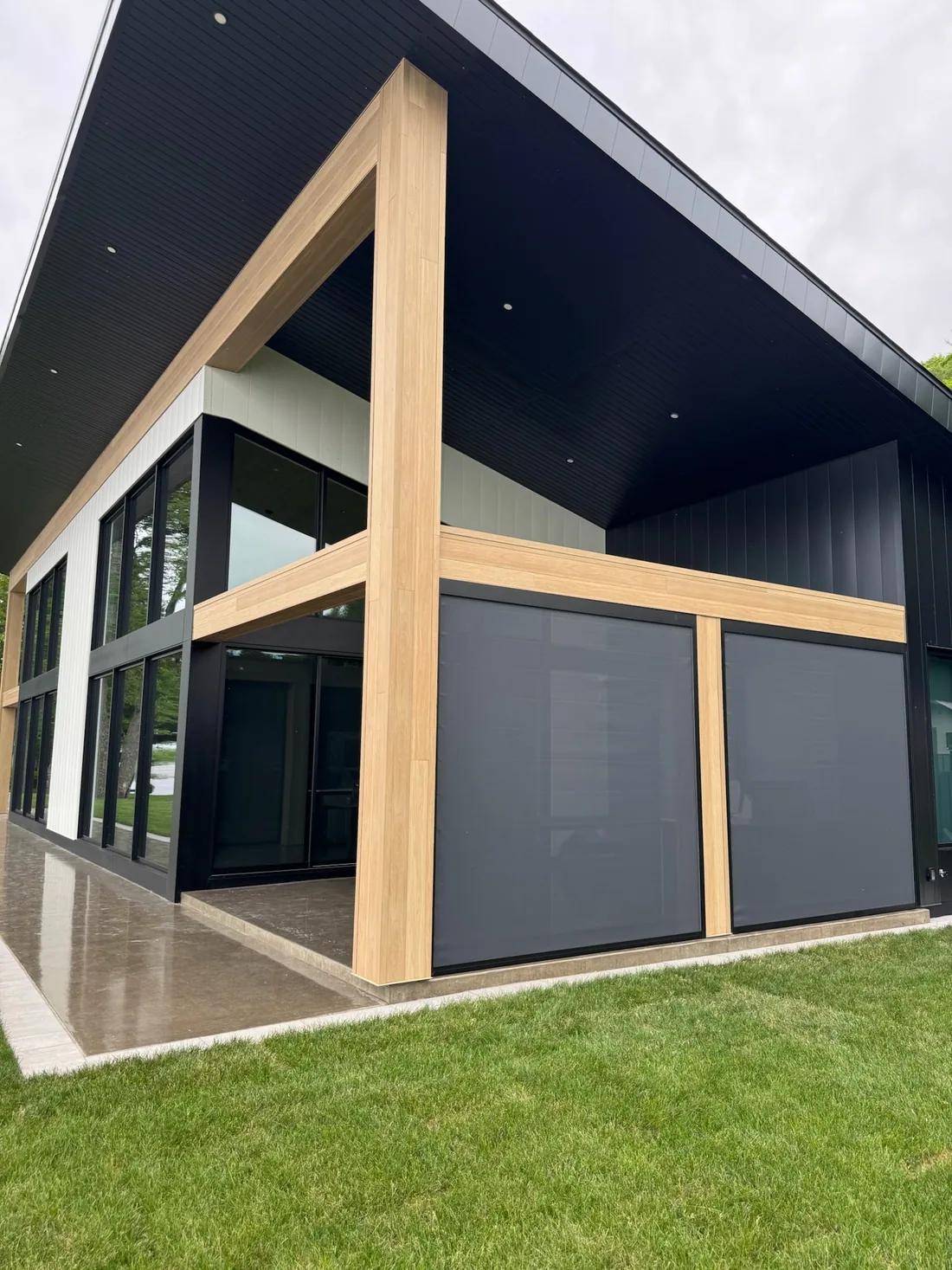 Deux toiles solaires descendues entre des poteaux de bois sur une résidence contemporaine à revêtement noir
