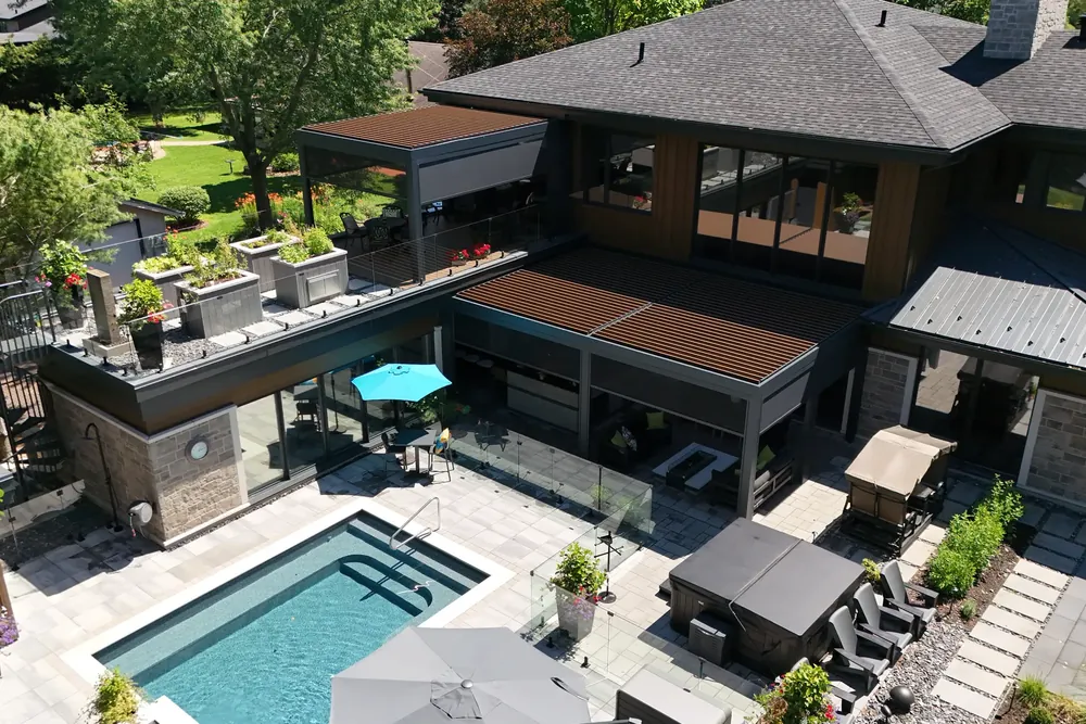 Vue aérienne d’une résidence : deux pergolas bioclimatiques à lames orientables couvrant un balcon et une terrasse, avec piscine creusée et spa