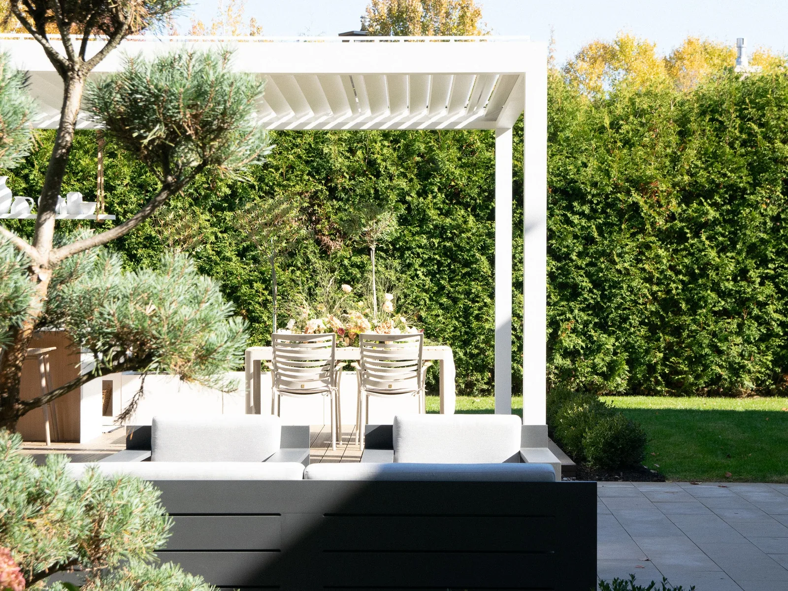 Pergola bioclimatique Capri blanche aux lames orientables, au-dessus d’un salon et d’une table de jardin.