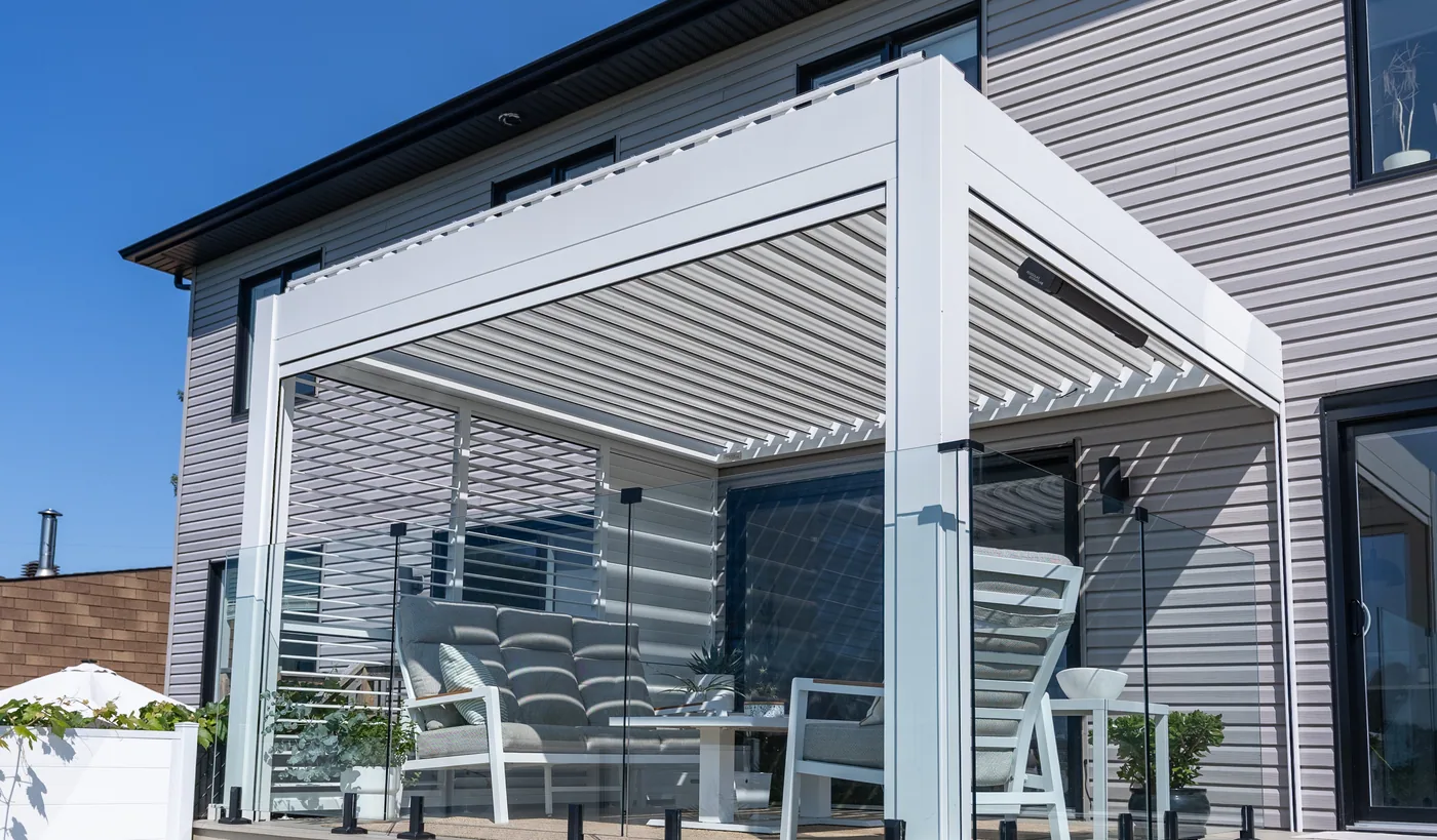 La pergola vue de la piscine : lames orientables, chauffe-terrasse sur la poutre et toile descendue contre la maison