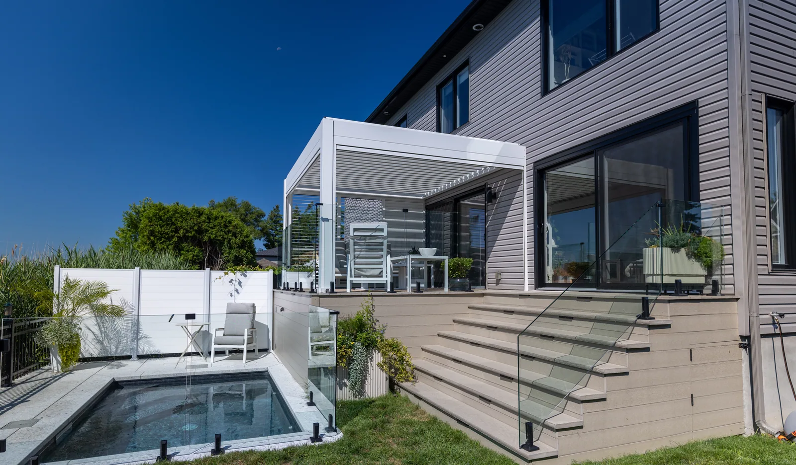 Pergola Provence blanche adossée à la maison, sur une terrasse surélevée au-dessus de la piscine creusée