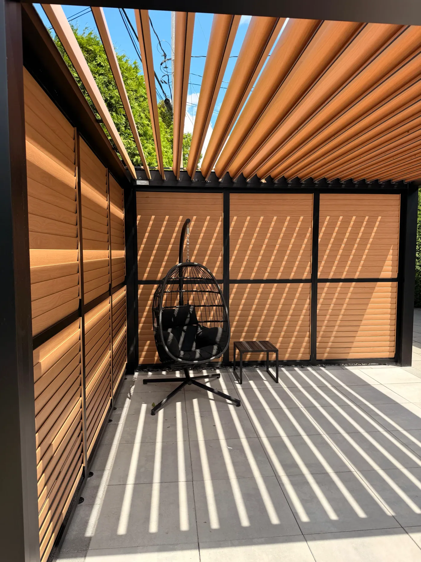 Sous la pergola : lames orientables fini bois, murs d’intimité et ombre rayée sur les dalles