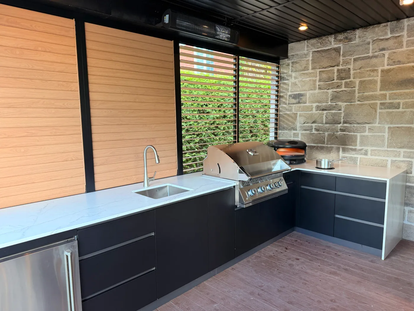 Cuisine extérieure en L sous la terrasse couverte, entre le mur à lamelles orientables et le mur de pierre