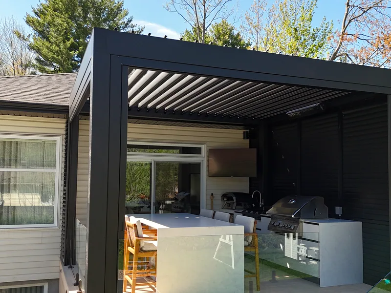 Black bioclimatic pergola against the house in Terrebonne, level with the roof edge, with an outdoor kitchen and a louvred privacy wall