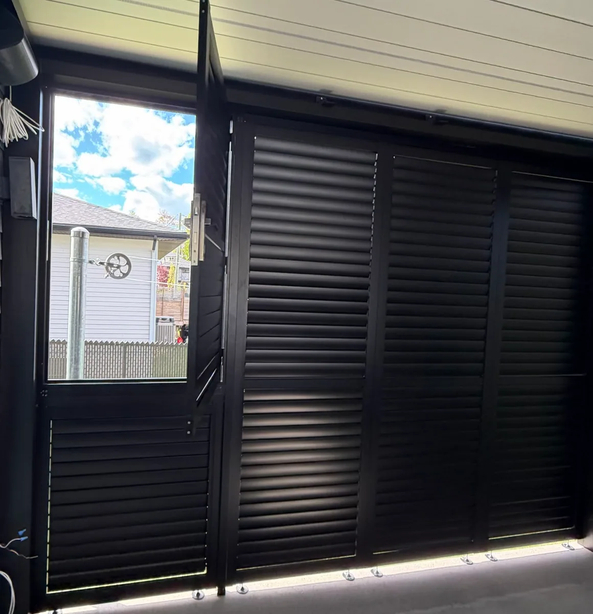 Louvred door standing open in the privacy wall: the clothesline and its pulley show through the opening