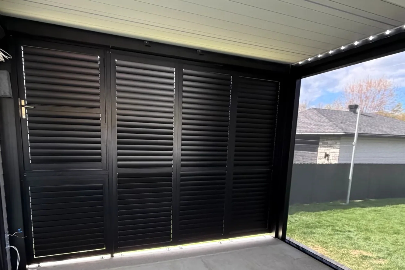 Black aluminum louvred privacy wall under the pergola, built-in door on the left, bay open onto the yard on the right