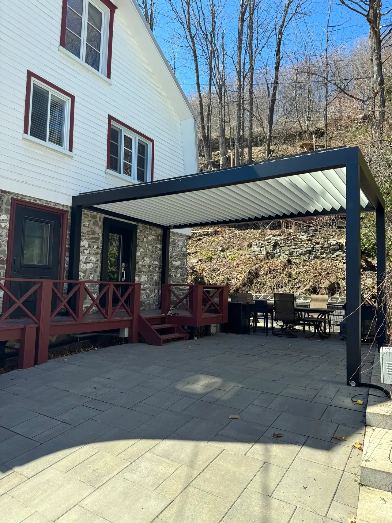 Pergola Capri autoportante à lames blanches et structure charbon, sur les pavés d’une maison ancestrale en pierre des champs
