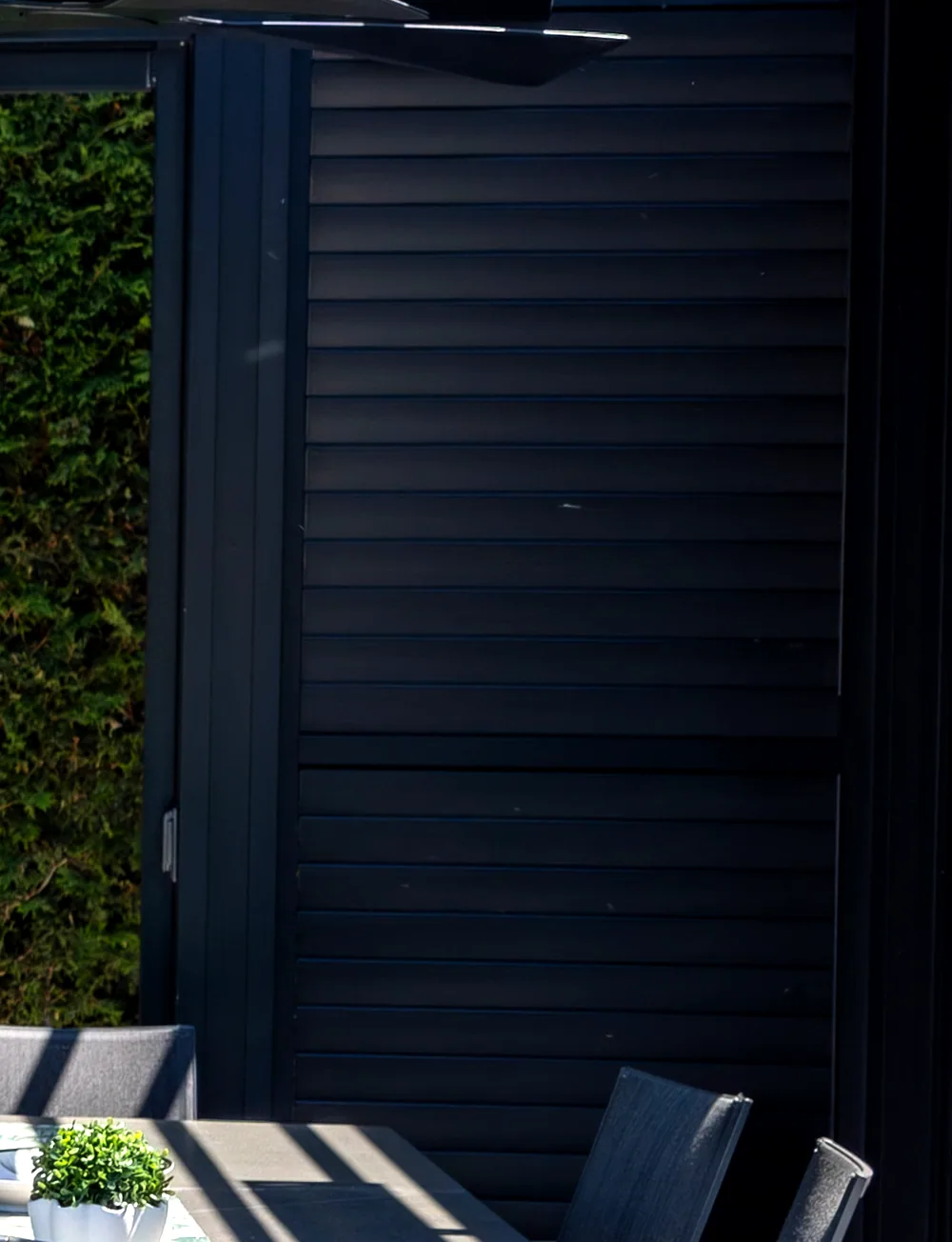 Black louvred privacy wall under the pergola, hinged door built in, handle on the stile