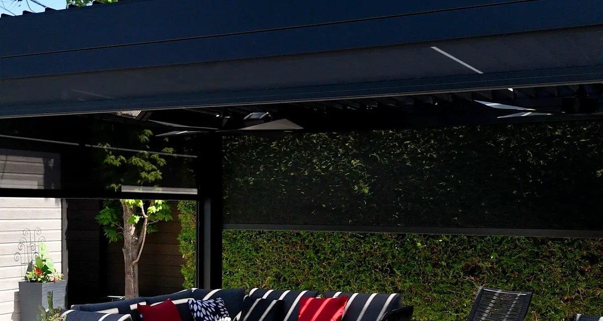 Solar shade lowered on the hedge side, under the louvred roof of the pergola