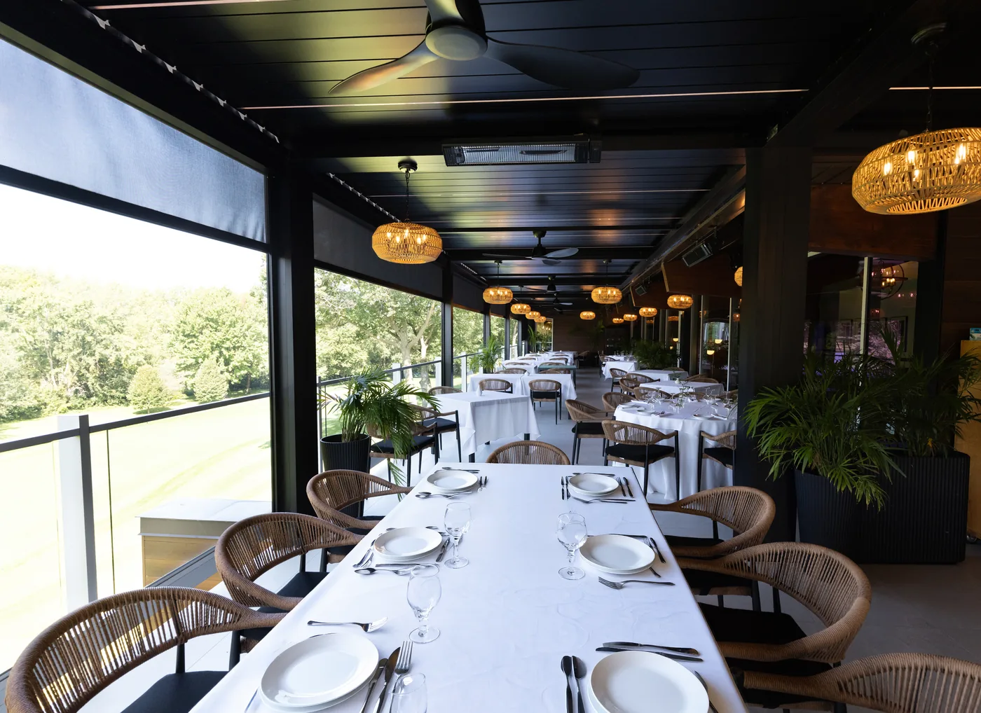 Ventilateur de plafond et chauffe-terrasse électrique fixés aux poutres noires, au-dessus des tables dressées